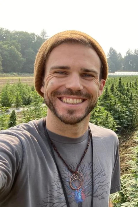 Logan smiles at the camera in front of a field of cannabis.