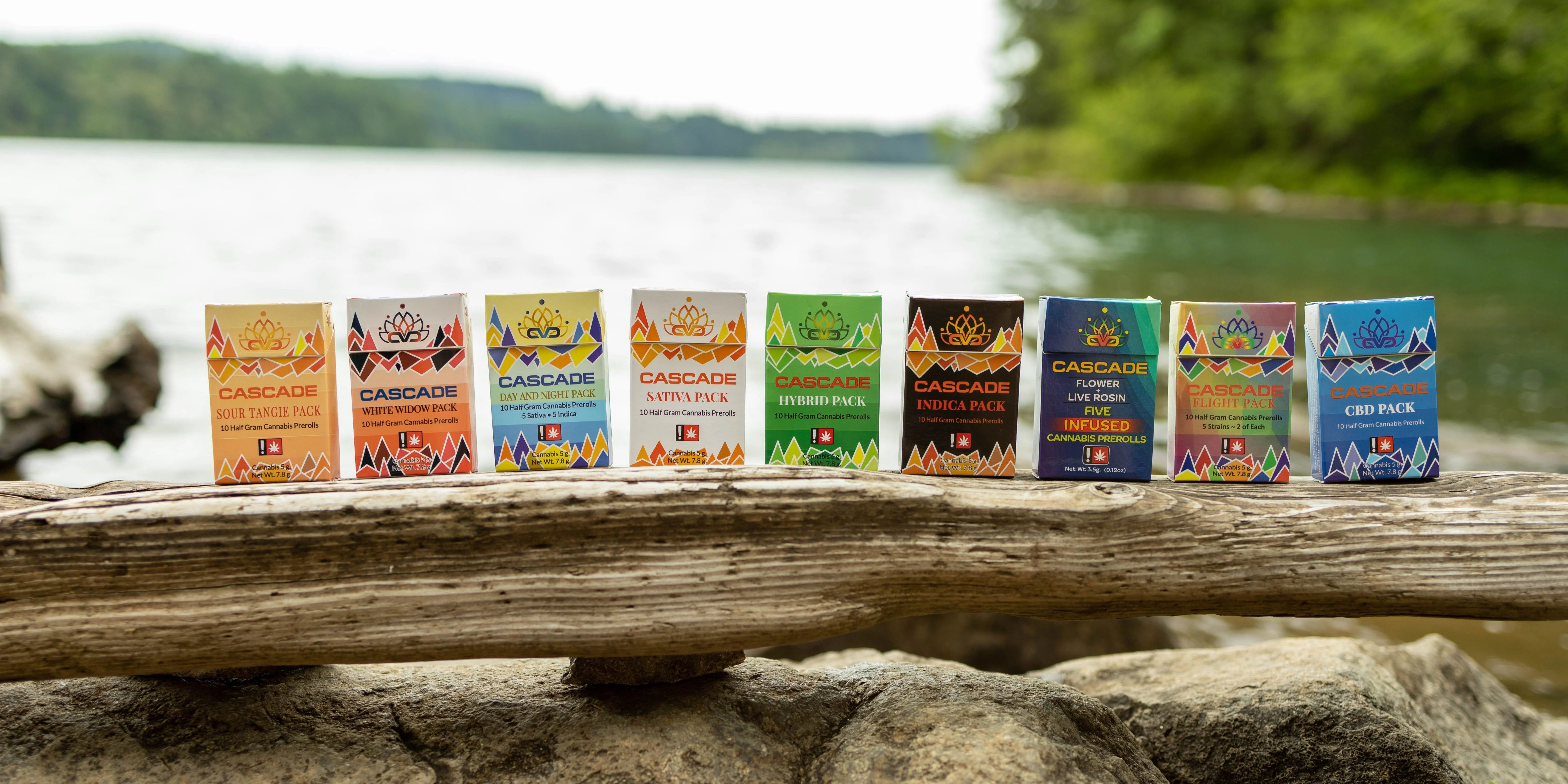 A variety of cartons of joints are lined up on a log by a river
