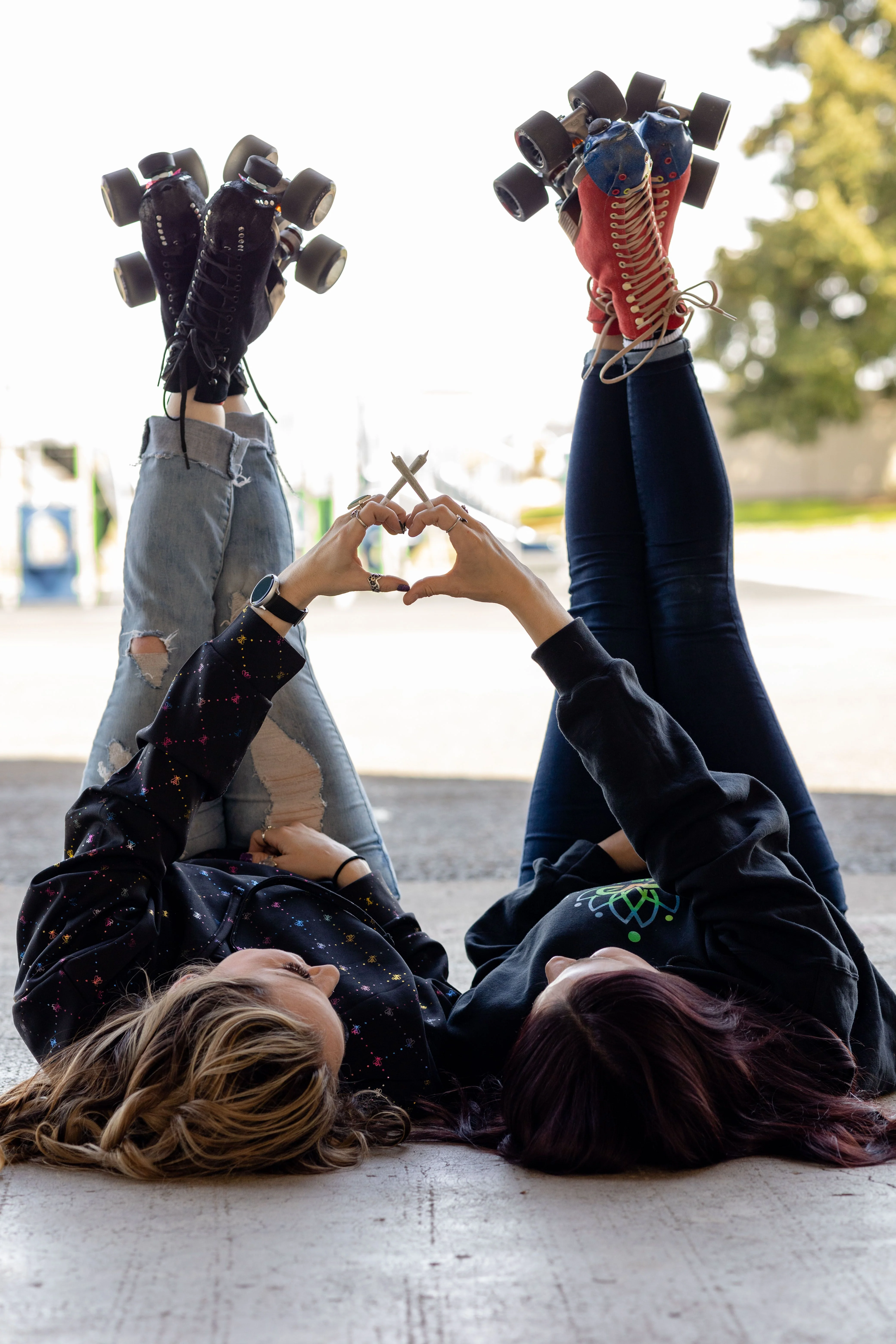Two people wearing roller skates form a heart with their hands, which are holding prerolled joints.